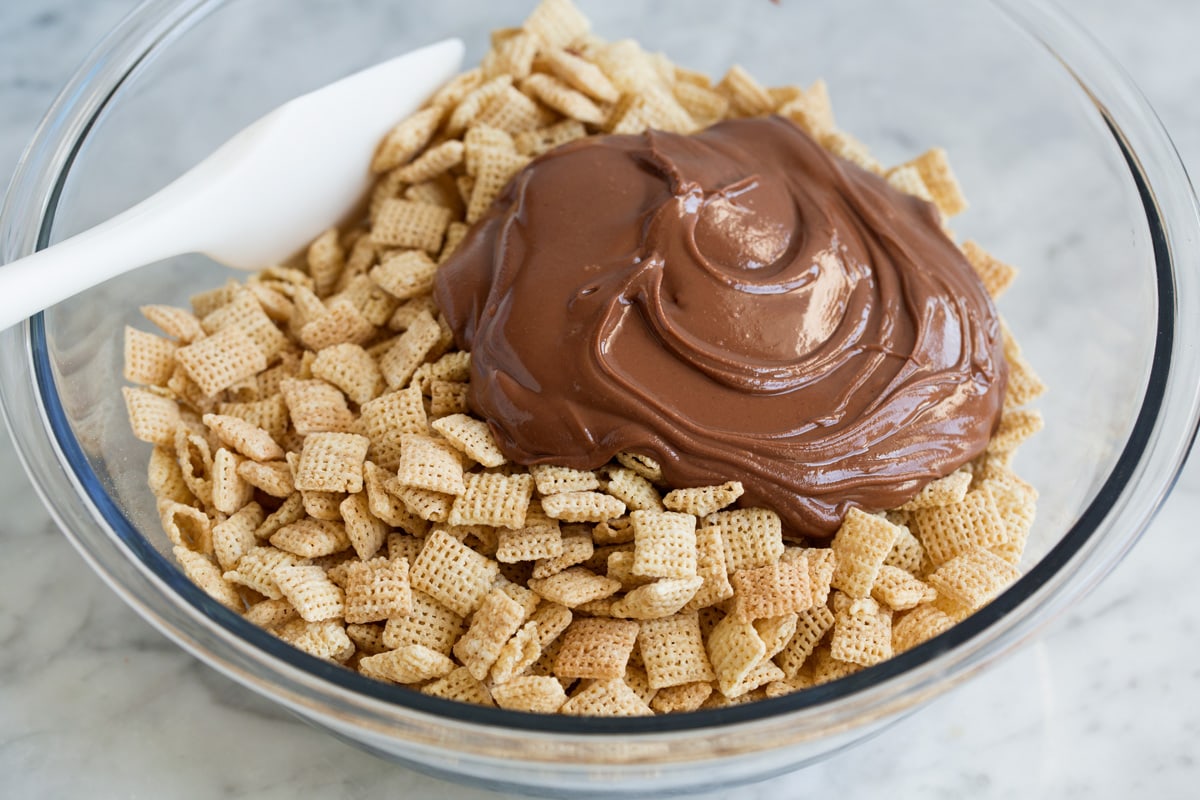 Adding chocolate mixture to chex cereal in a mixing bowl.