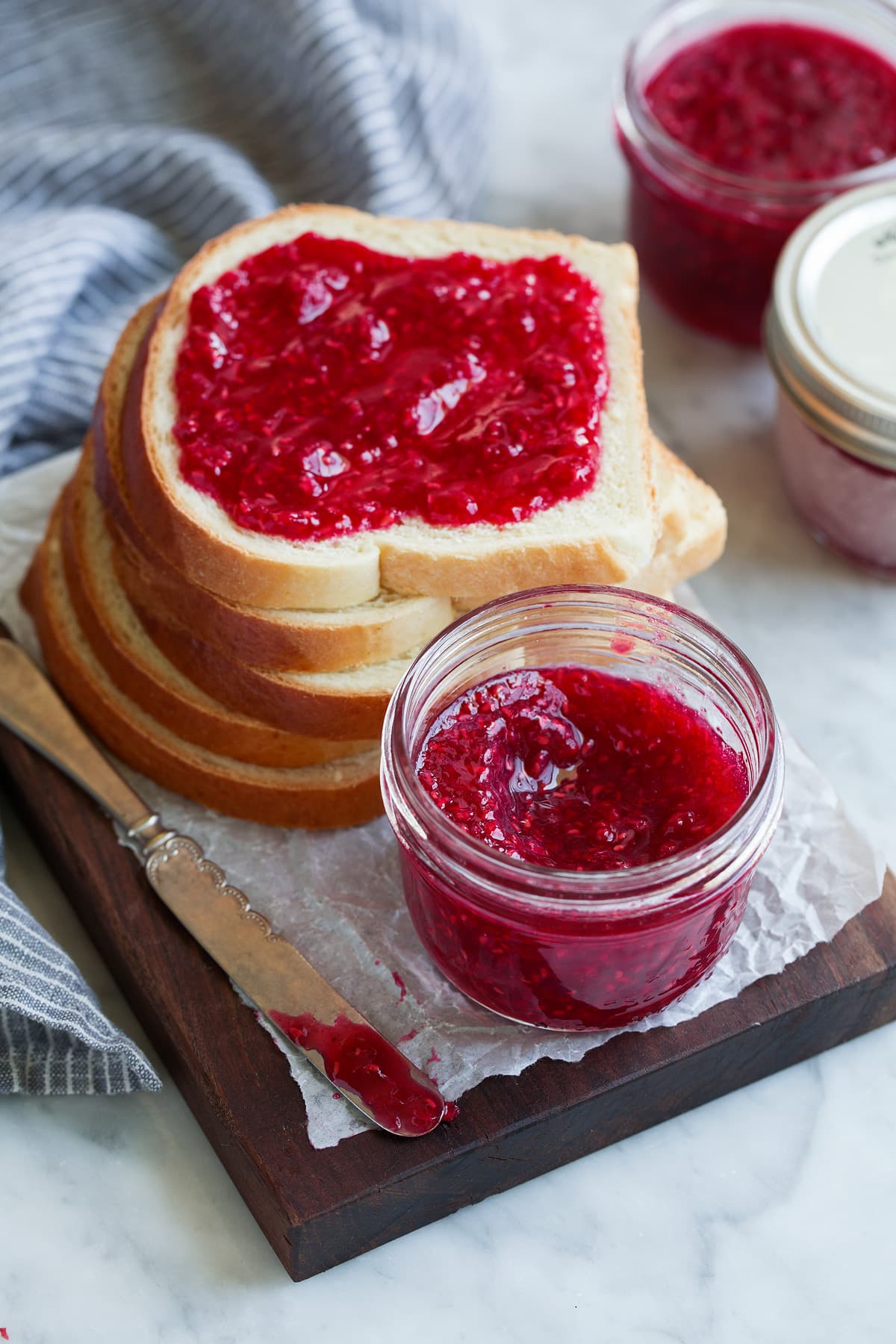 Homemade jam in a jar next to a stack of bread with top slice slathered in jam.