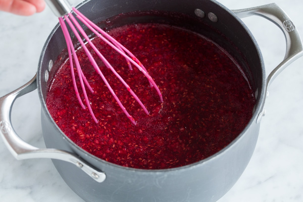 Whisking raspberries into sugar mixture in saucepan,