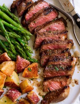 Marinated grilled steak on a serving plate with a side of asparagus and potatoes.