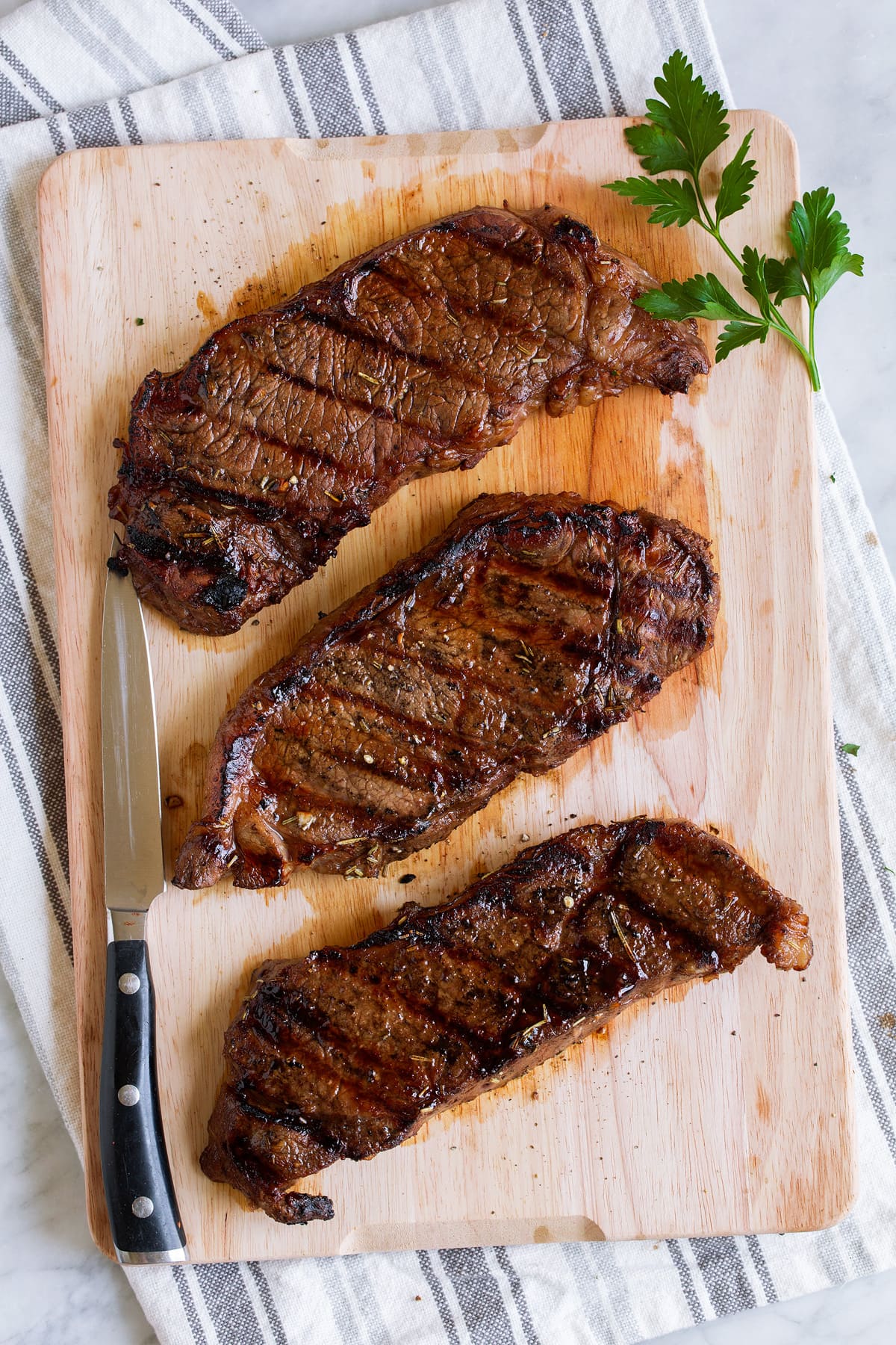 Three steaks on a wooden cutting board.