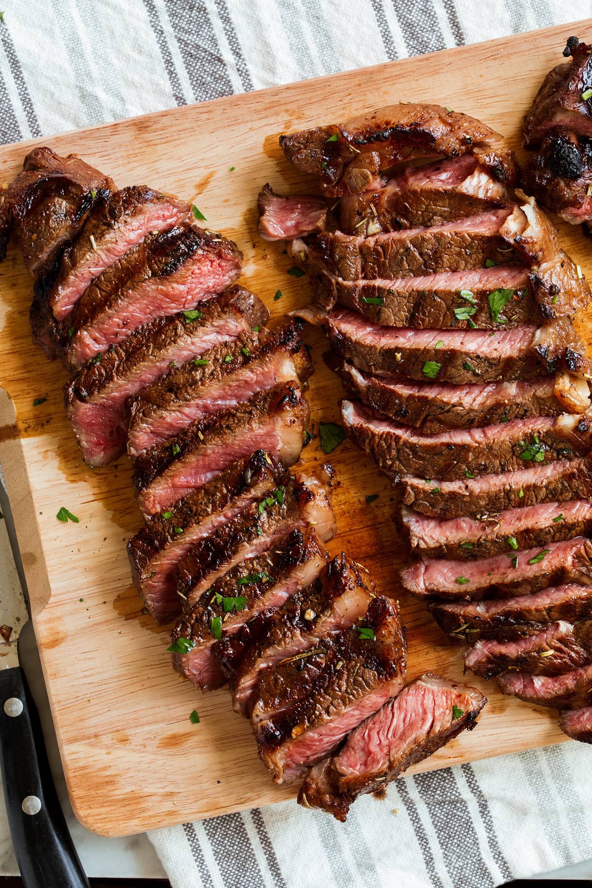 Two sliced new york strip steaks on a wooden cutting board. 