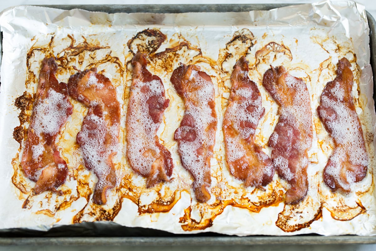 Strips of oven cooked bacon on a baking sheet lined with foil.