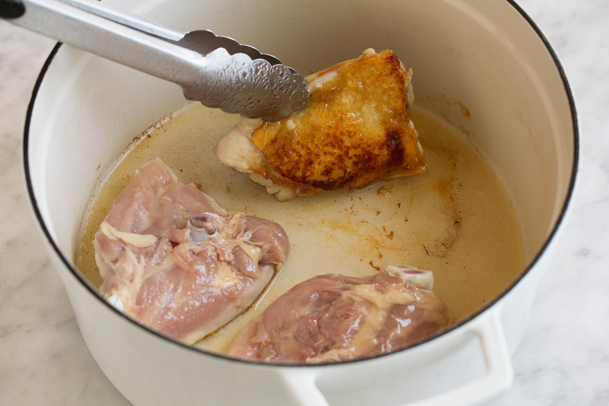 browning three chicken thighs in vegetable oil in a pot. Showing how to make chicken adobo.
