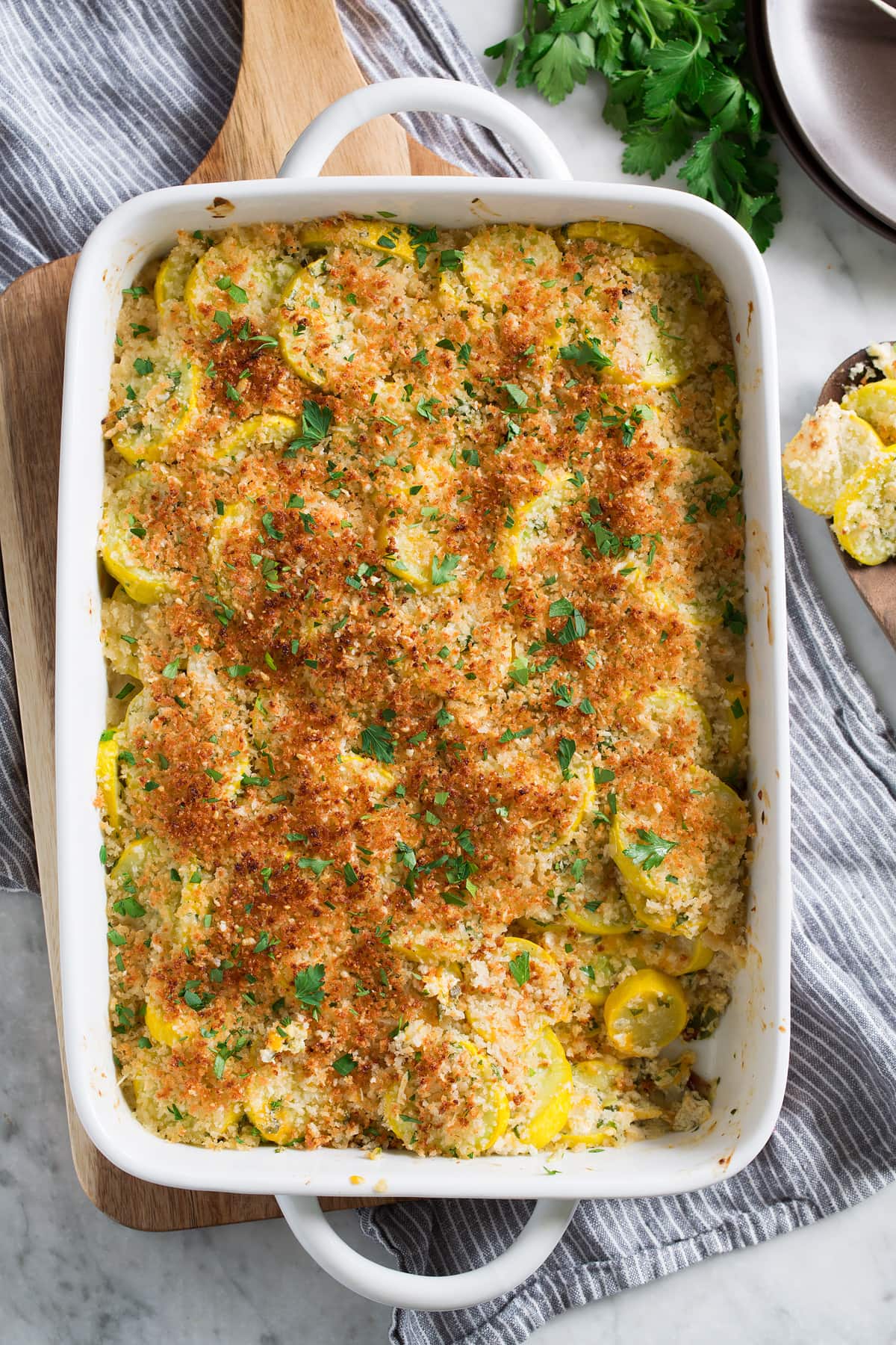 Yellow squash casserole in a white baking dish with one scoop removed to show filling.