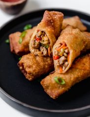 Egg rolls stacked on a black plate with one cut in half to show exterior.