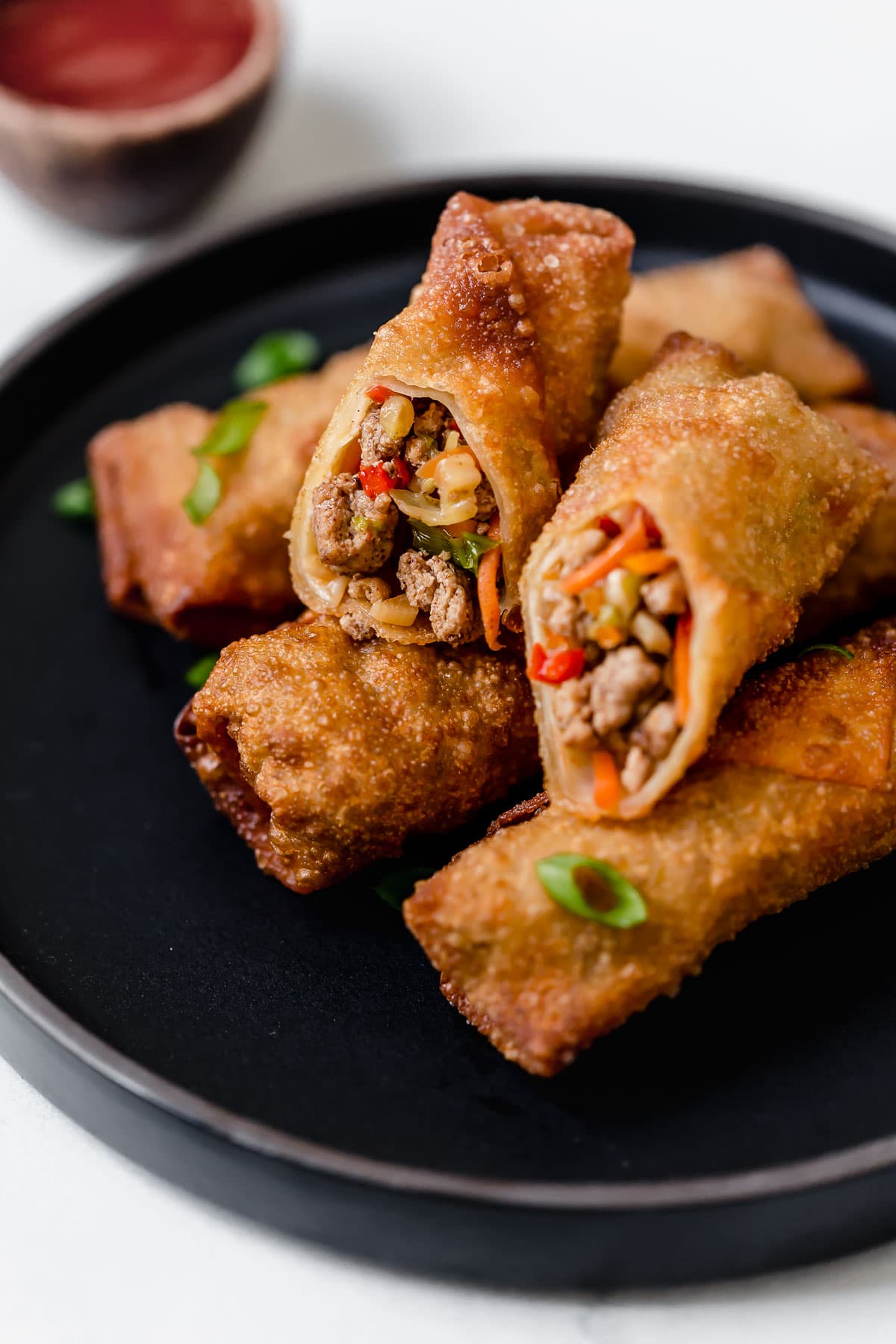 Egg rolls stacked on a black plate with one cut in half to show exterior.