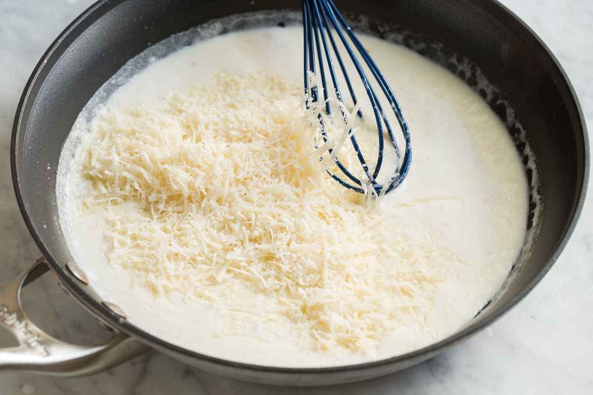 Adding shredded parmesan to cream mixture in skillet.