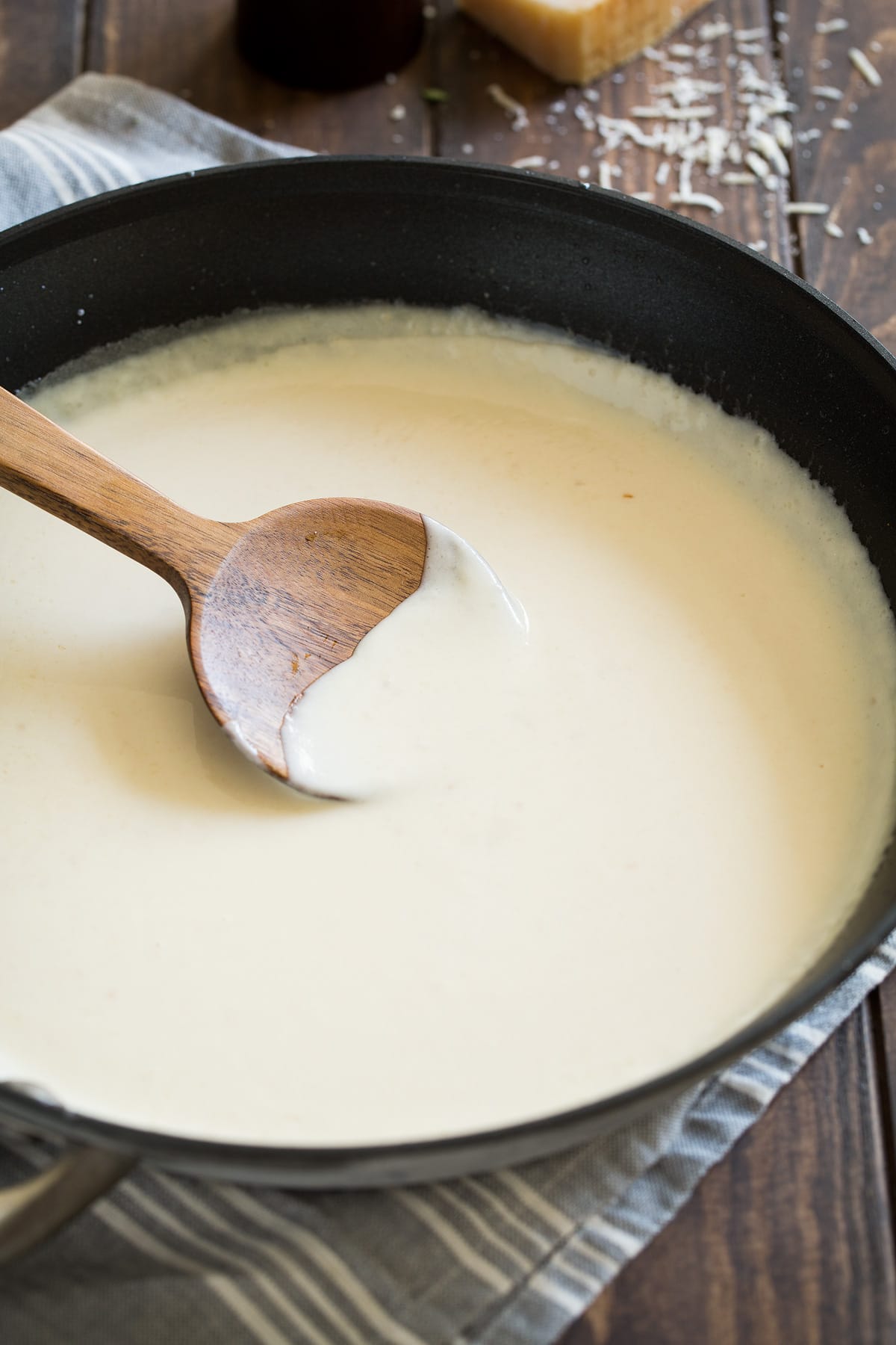 Alfredo sauce in a skillet with a wooden spoon.