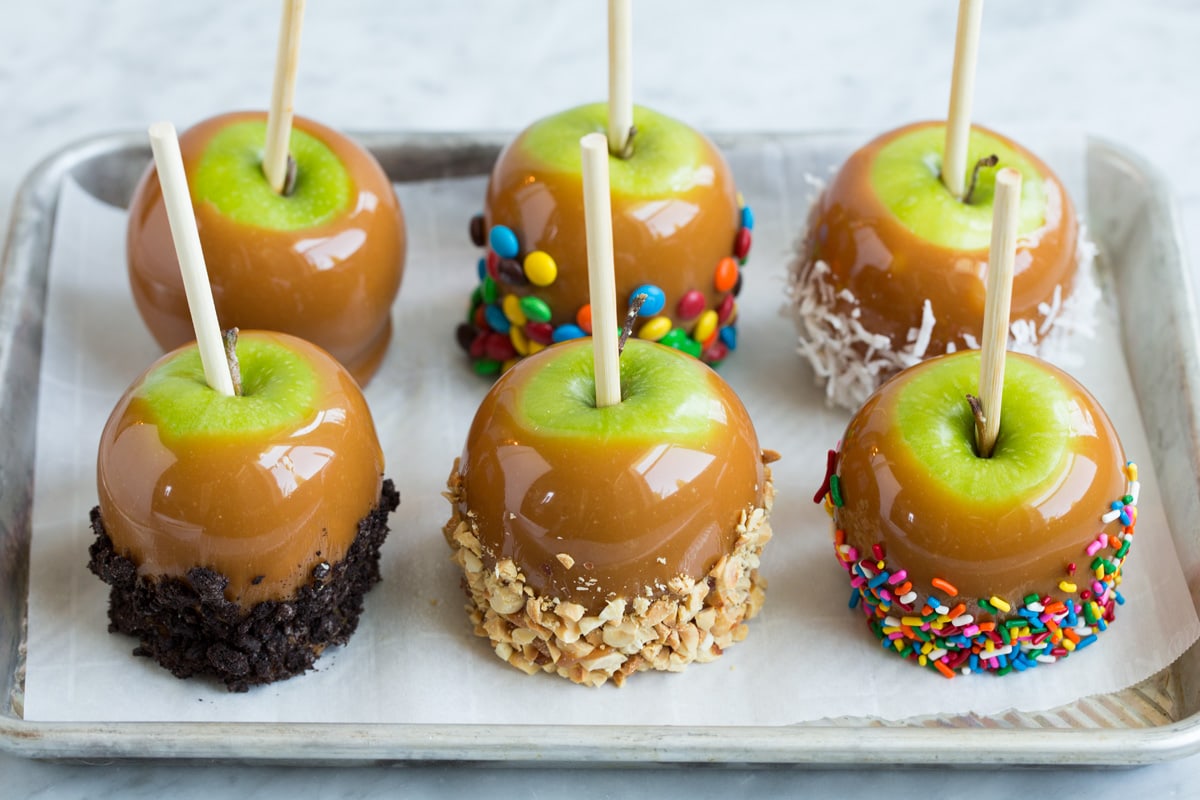 Six caramel apples on a baking sheet lined with parchment paper.