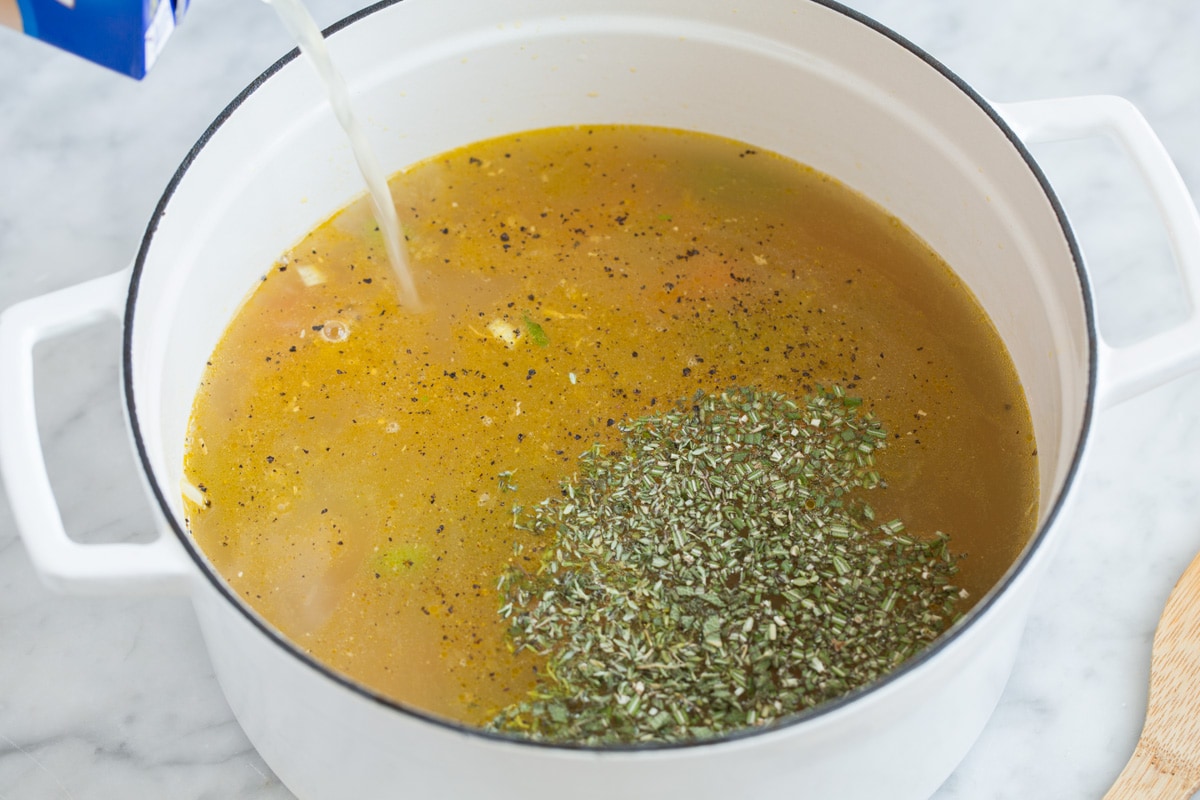 Pouring broth and herbs into pot.
