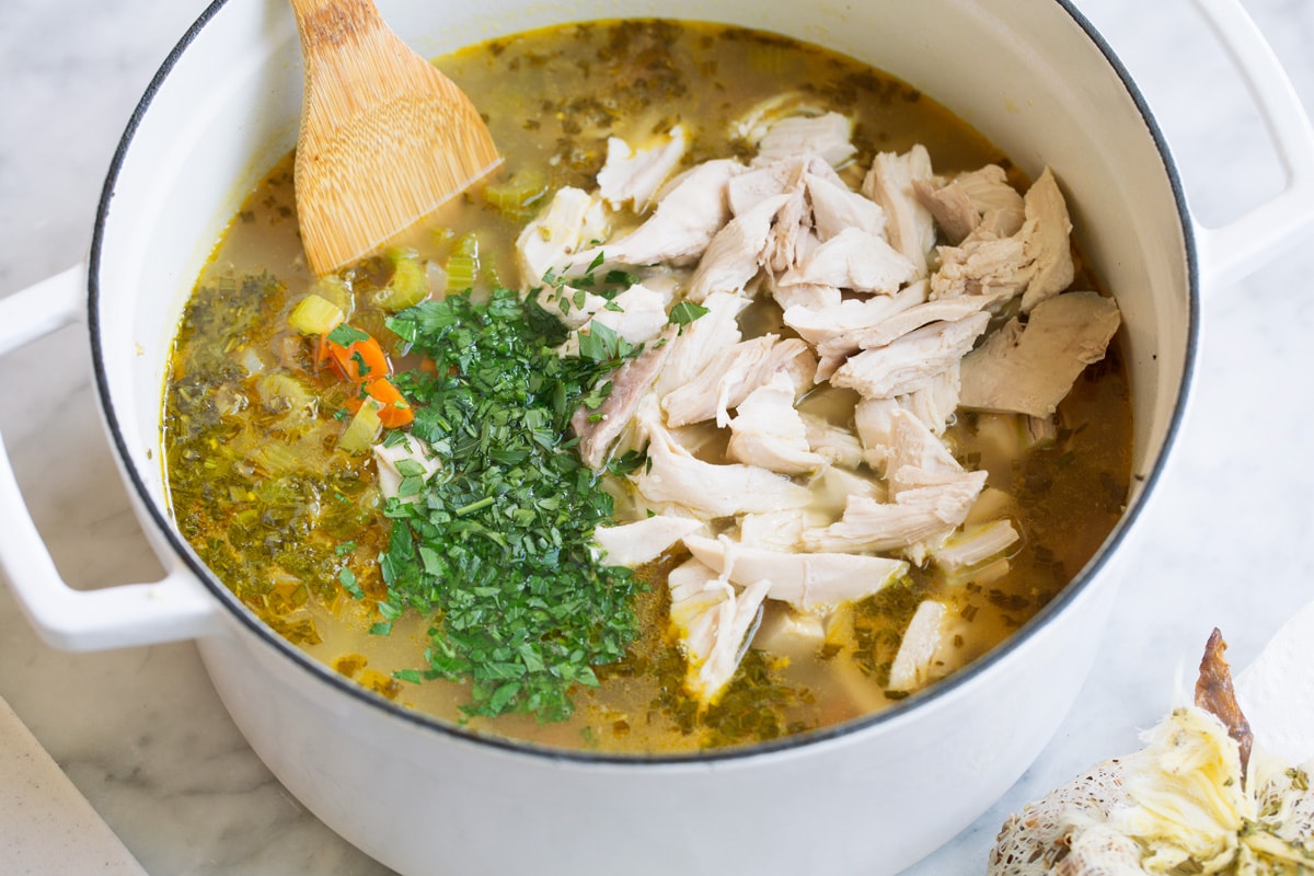 Adding chicken and more fresh herbs to soup.
