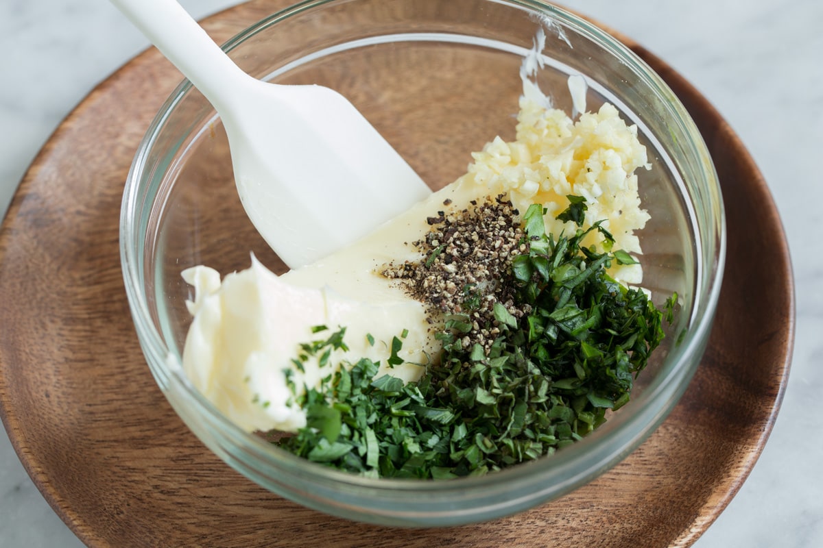 Mixing butter, herbs and garlic in a glass mixing bowl.