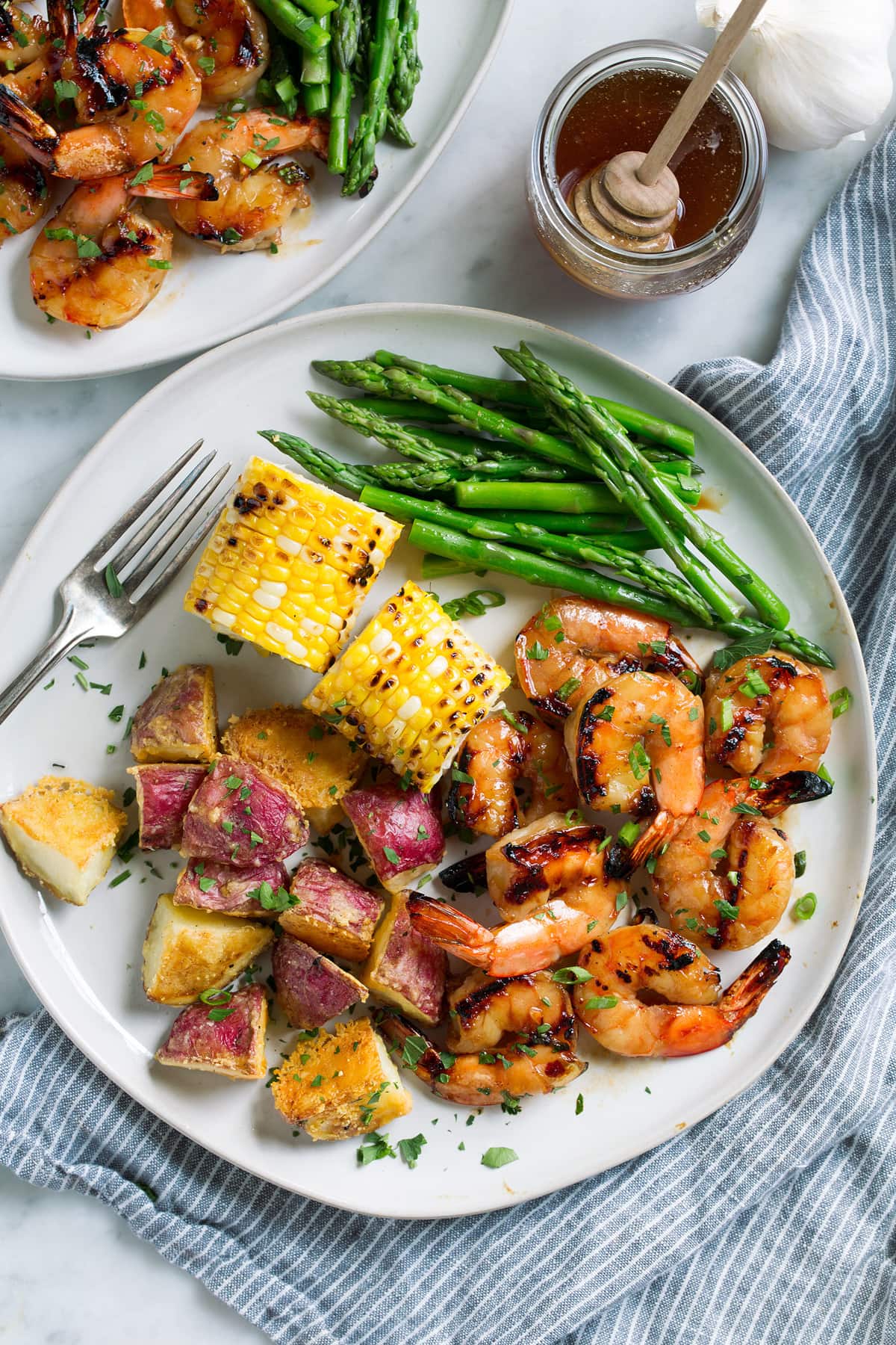 Grilled shrimp on a plate with a side of grilled corn, steamed asparagus and roasted potatoes.