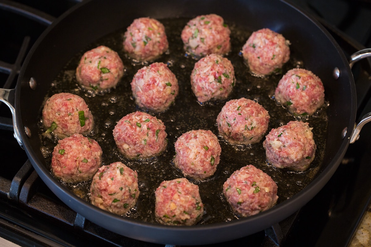 Frying raw meatballs in olive oil in a large skillet.