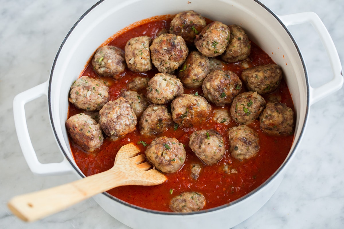 Tossing meatballs with marinara sauce in a pot.