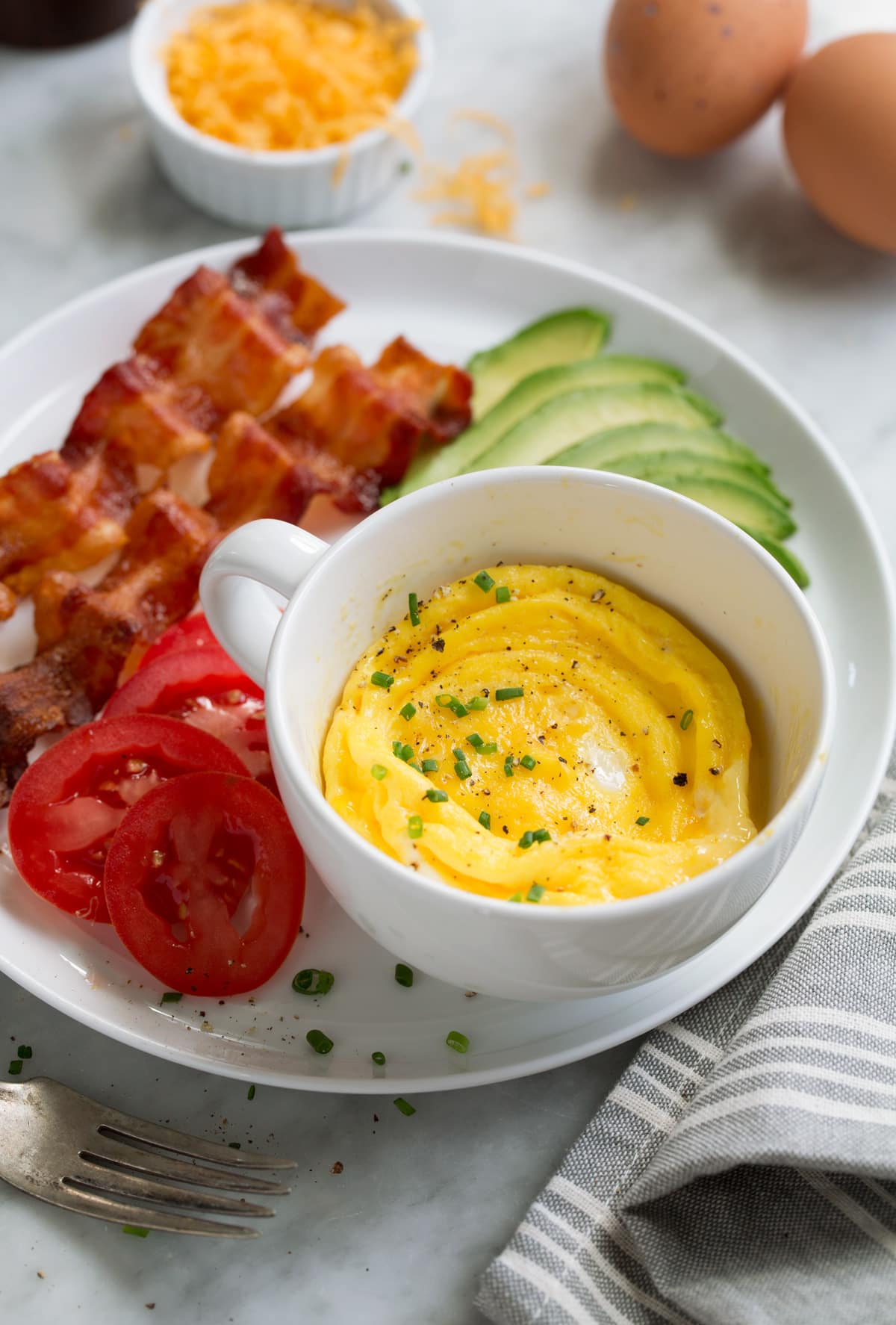 Microwave eggs with bacon, tomatoes and avocado to the side on a plate.