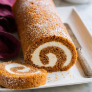 Pumpkin Roll on a white platter with a slice cut to show swirled cream cheese filling.