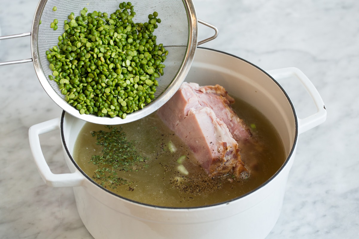 Adding split peas and ham to soup mixture in pot.