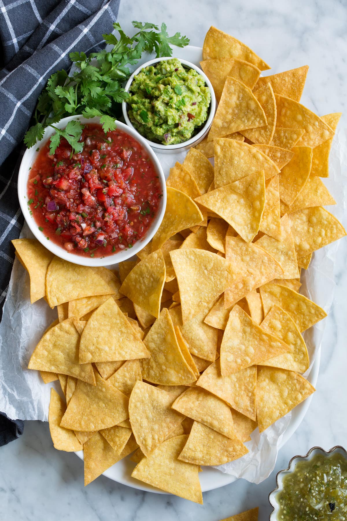 Platter full of homemade tortilla chips with a side of salsa, guacamole and salsa verde.
