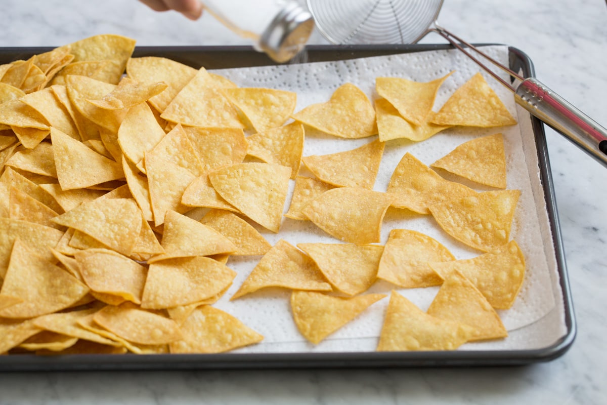 Draining fried tortilla chips on a baking sheet lined with paper towels.