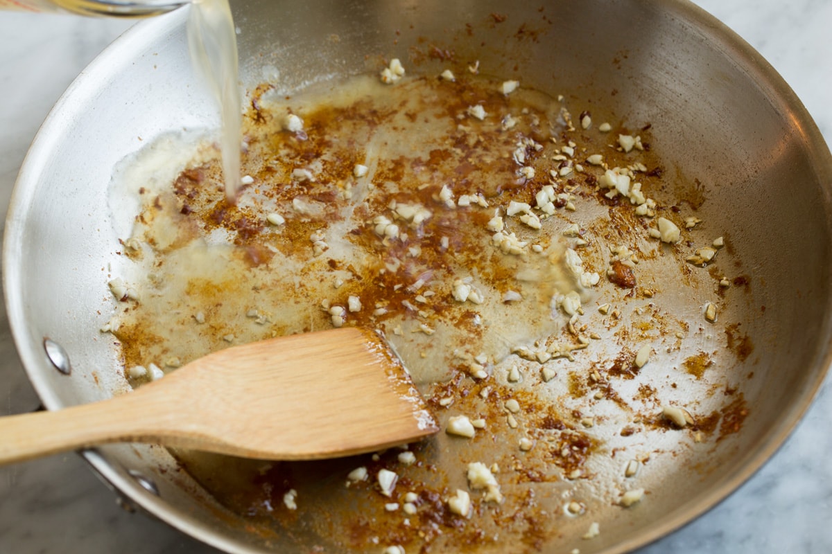 Adding chicken broth and lemon to arlic and browned bits in the bottom of a skillet.