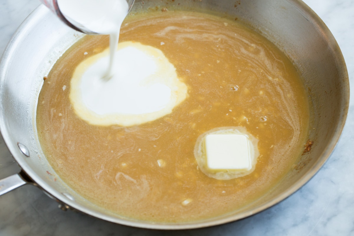 Stirring cream and butter into chicken piccata sauce in a skillet.