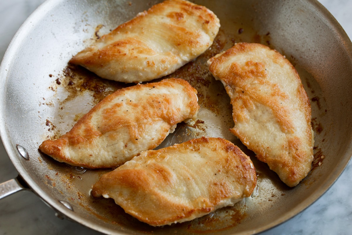 Four fully cooked chicken cutlets in a skillet.