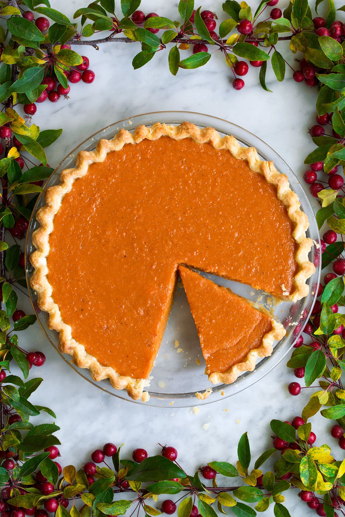 Sweet potato pie with one sliced cut. It's decorated with berry tree branches around it.
