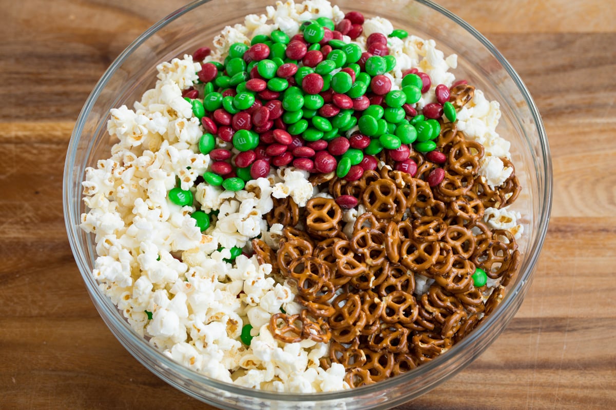 Adding pretzels and red and green m & m's to popcorn in bowl.