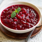 Cranberry Sauce in a serving bowl set over a wooden platter. Sauce garnished with fresh mint.