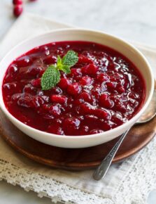 Cranberry Sauce in a serving bowl set over a wooden platter. Sauce garnished with fresh mint.