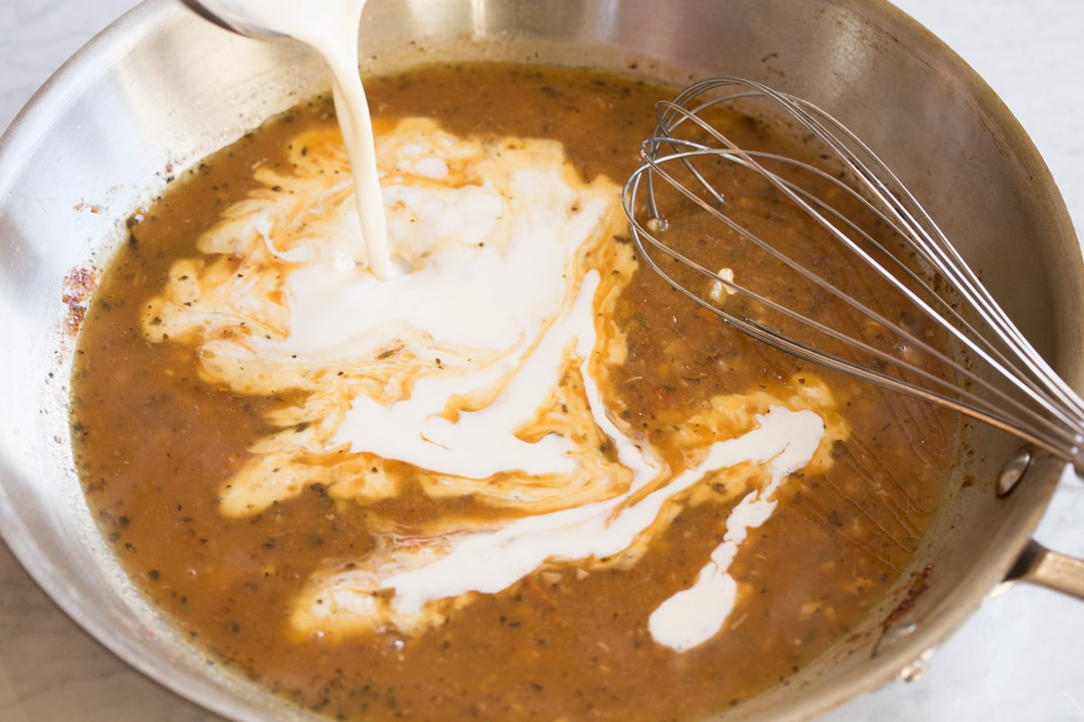 Pouring cream into sauce mixture in skillet.