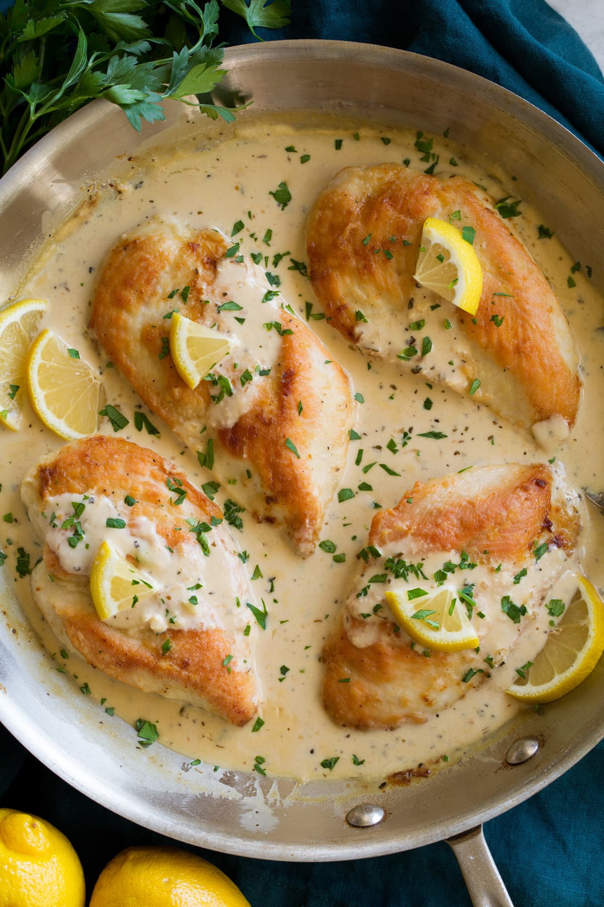 Four pan seared chicken breasts in a skillet with lemon romano sauce.