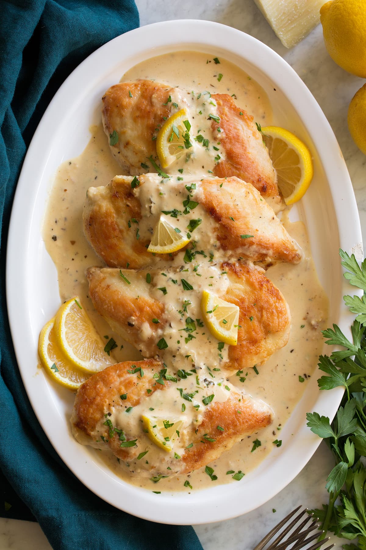Platter of four pan seared chicken breasts with creamy lemon romano sauce on top.