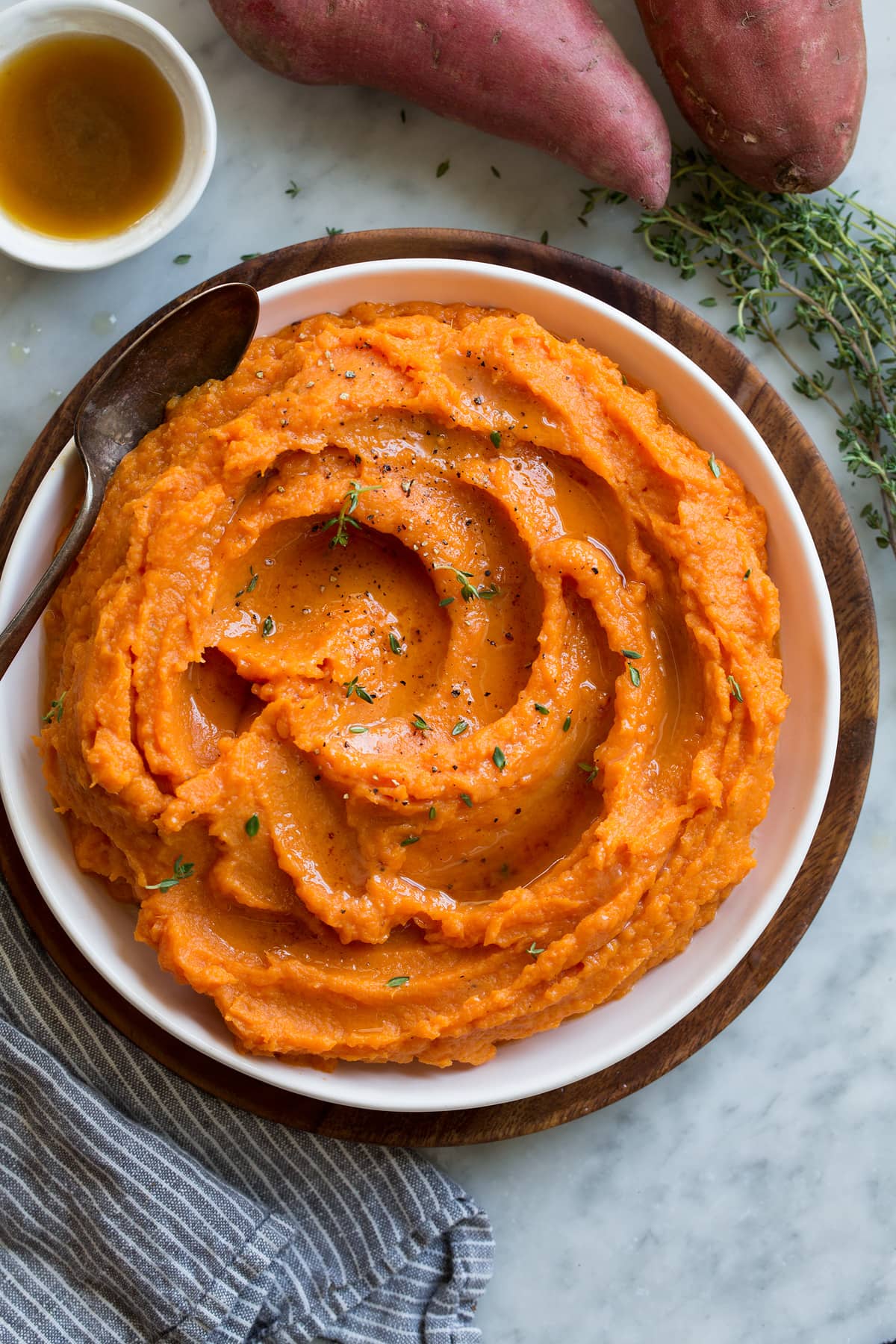 Overhead image of mashed sweet potatoes in a white serving bowl set over a wooden plate.