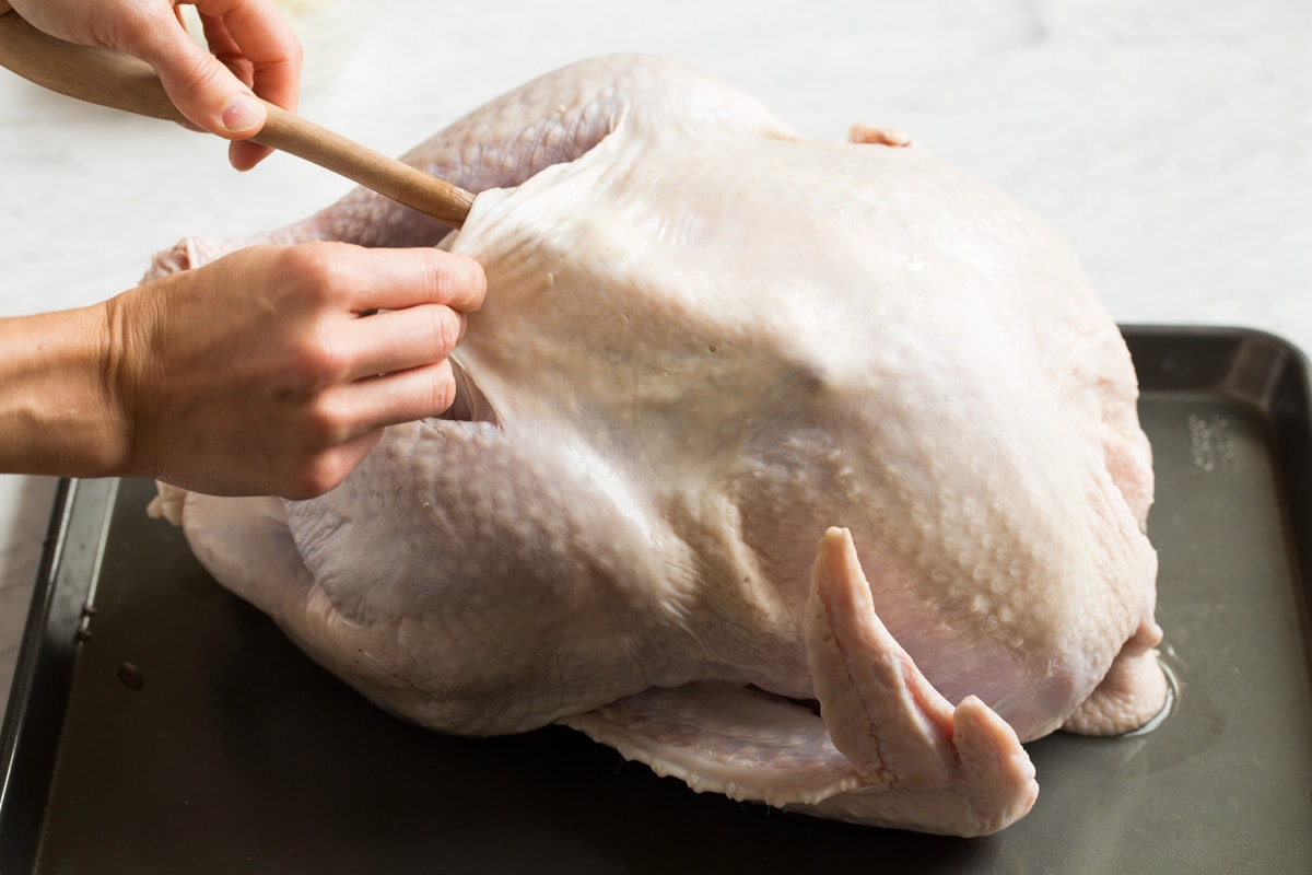 Separating turkey skin from breast using the back end of a wooden spoon.