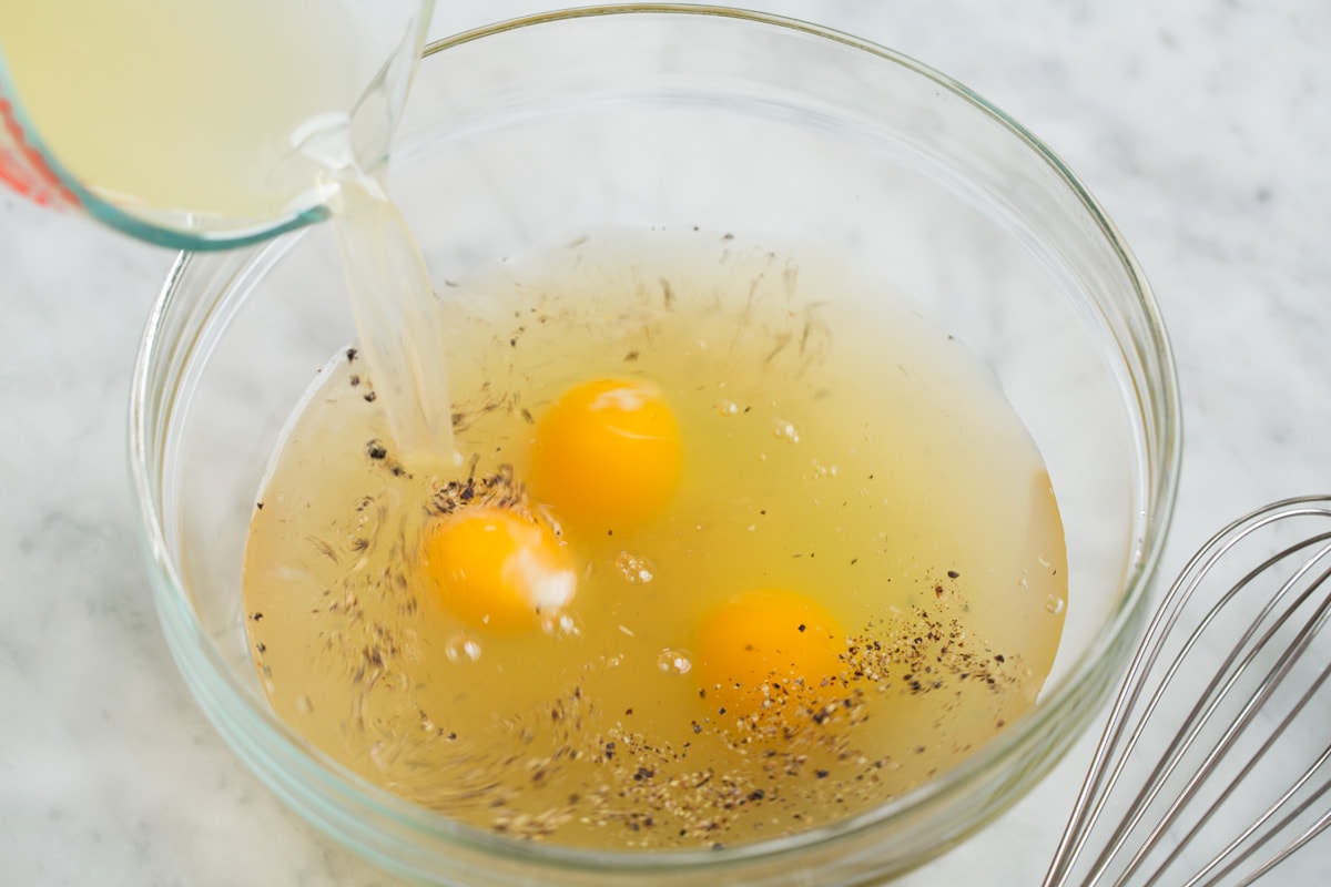 Mixing eggs, seasoning and broth in a glass mixing bowl.