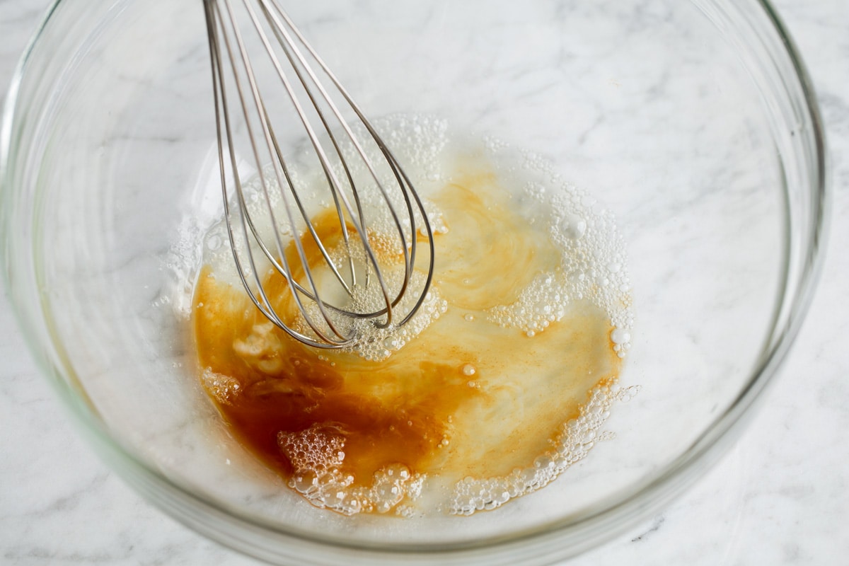 Mixing egg white and vanilla extract with a whisk in a glass bowl.