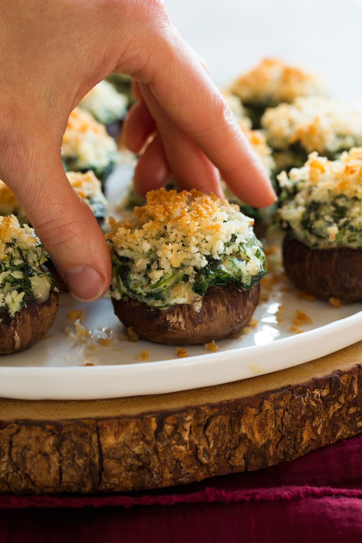 Hand picking up a stuffed mushrooms filled with cream cheese, shredded cheeses and spinach.