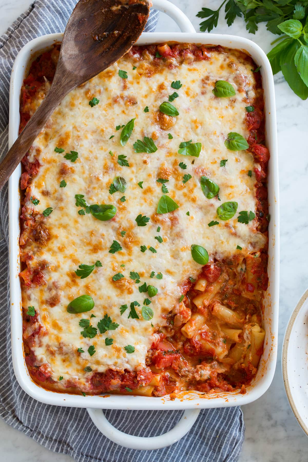 Baked Ziti in a casserole dish shown after baking with a lightly golden browned cheese topping. One scoop is removed to show interior.