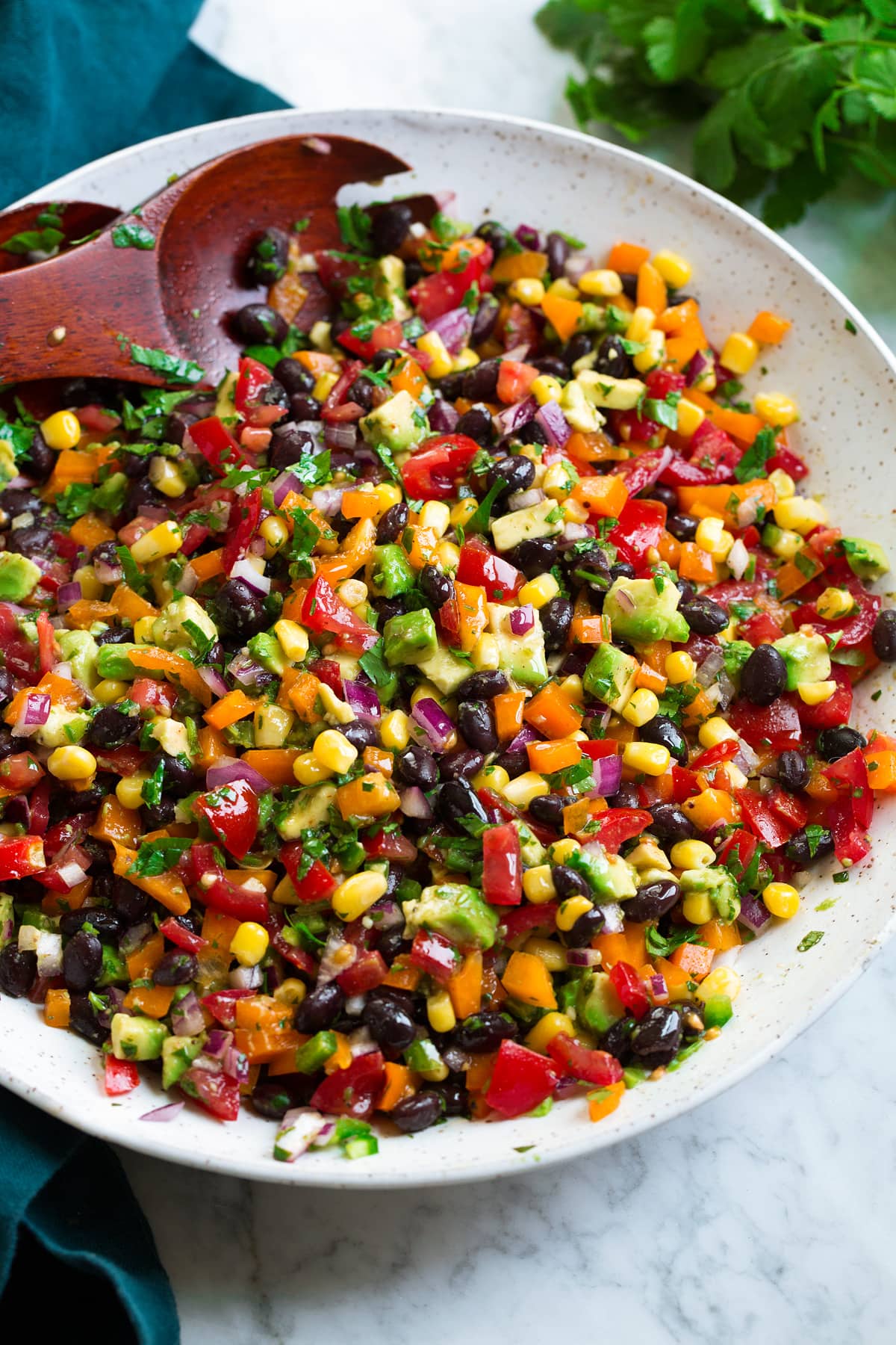 Black bean and corn salad in a white salad bowl with wooden serving spoons.