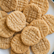 3 Ingredient Peanut Butter Cookies laying stacked on top of each other on a white serving plate.