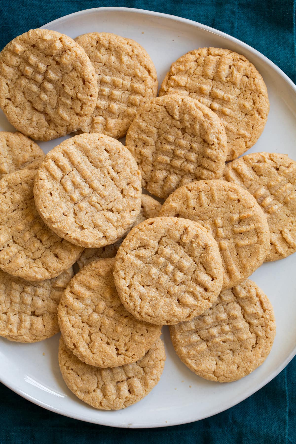 3 Ingredient Peanut Butter Cookies laying stacked on top of each other on a white serving plate.