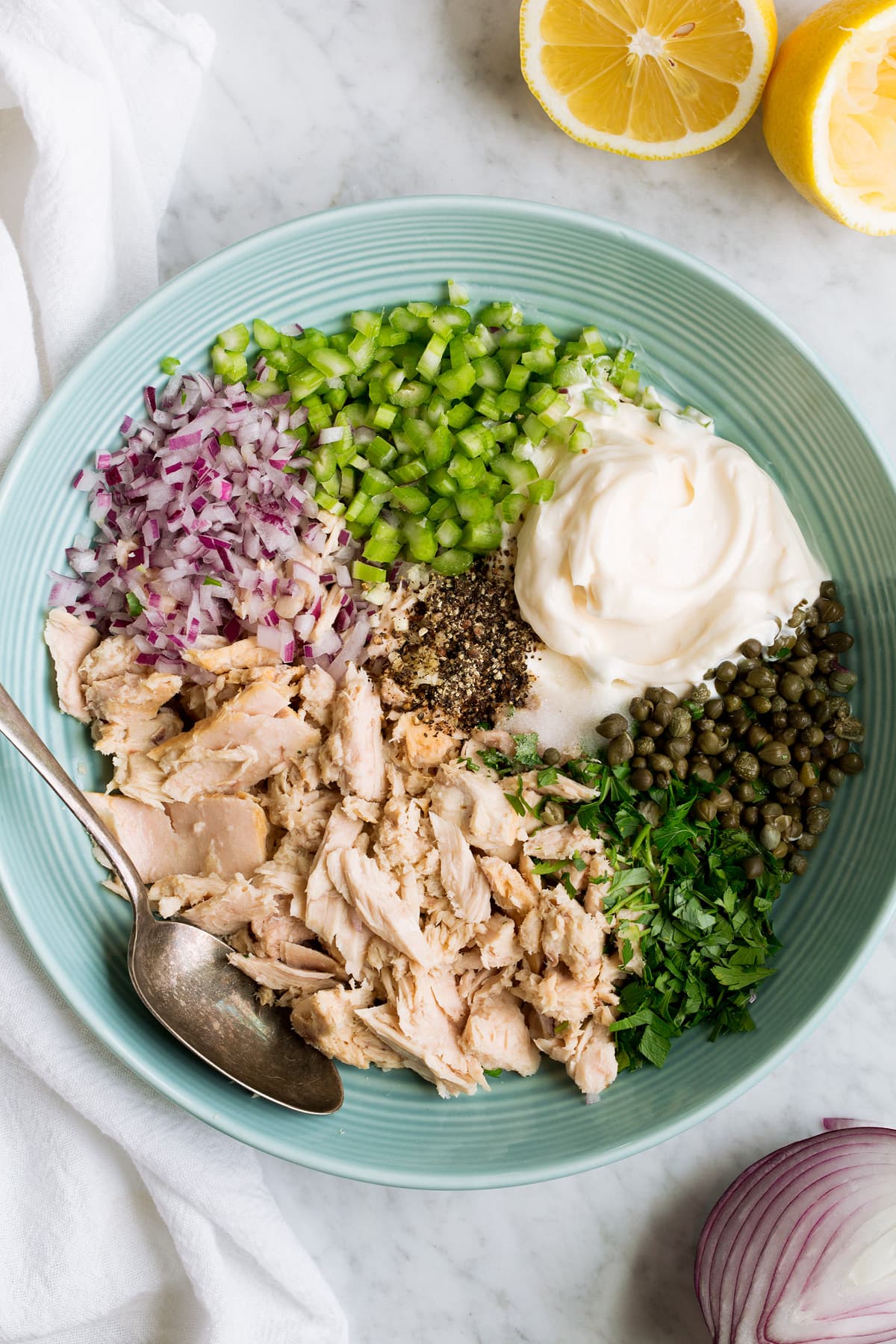 Image of tuna, parsley, red onion, celery, mayonnaise, lemon juice, capers, salt and pepper in a mixing bowl.