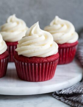 Cream cheese frosting shown piped over red velvet cupcakes.