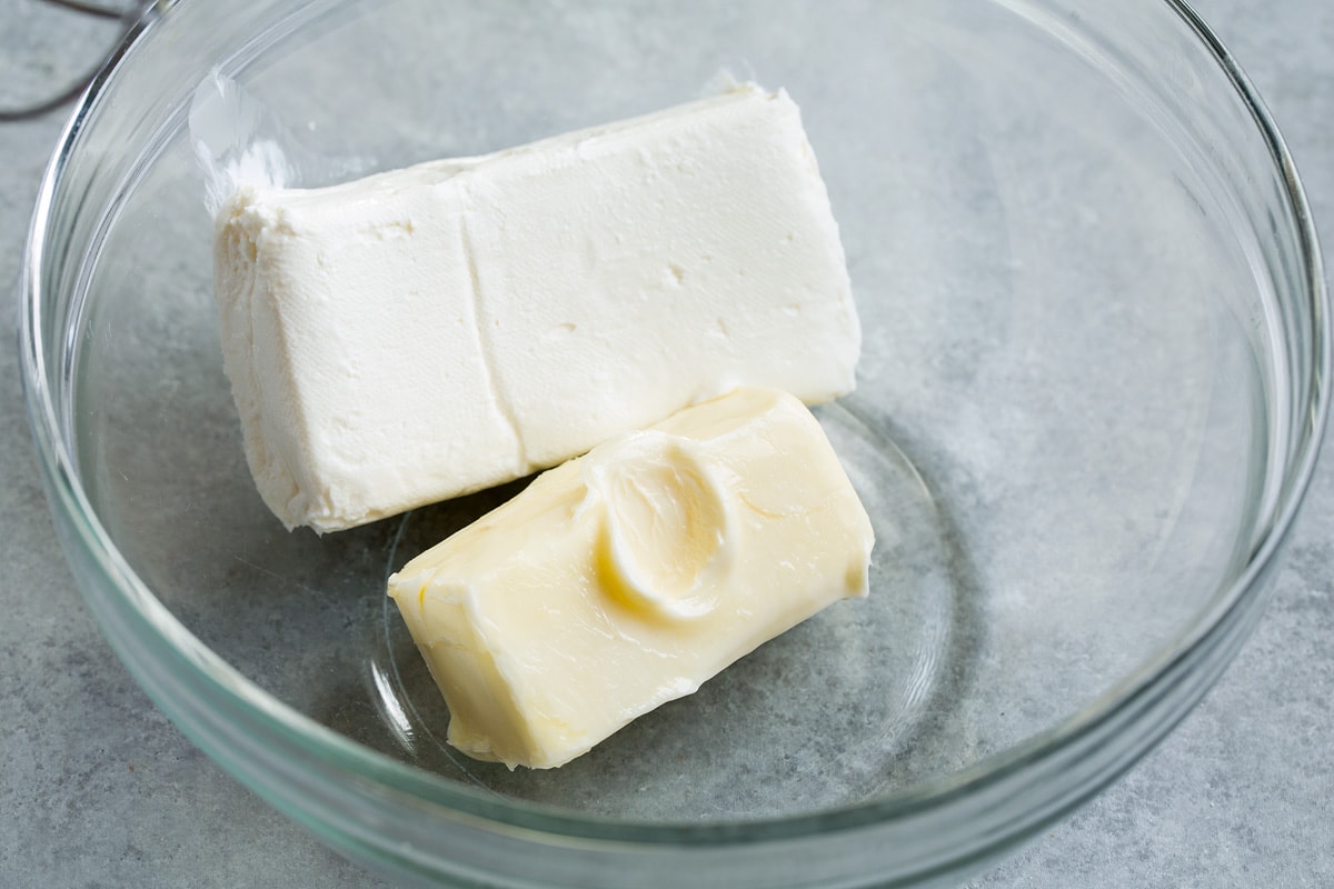 Block of cream cheese and butter in a glass mixing bowl.