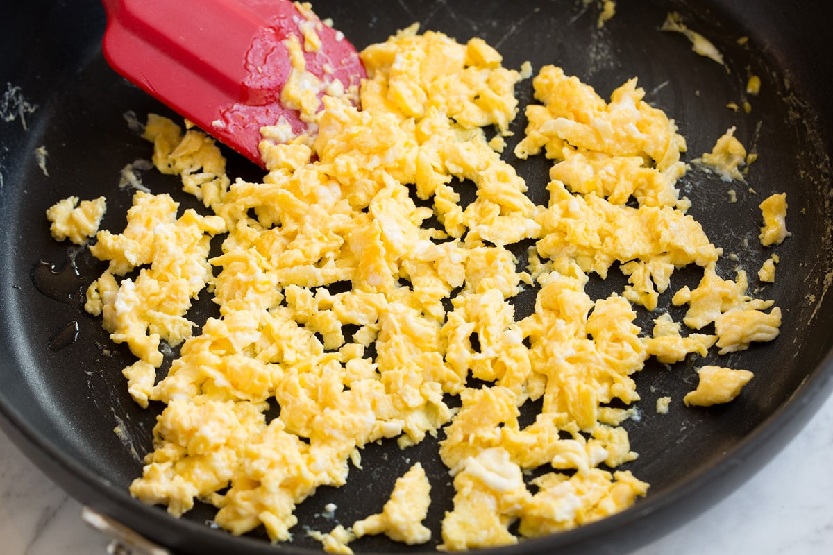 Scrambling and cooking eggs in a large skillet.