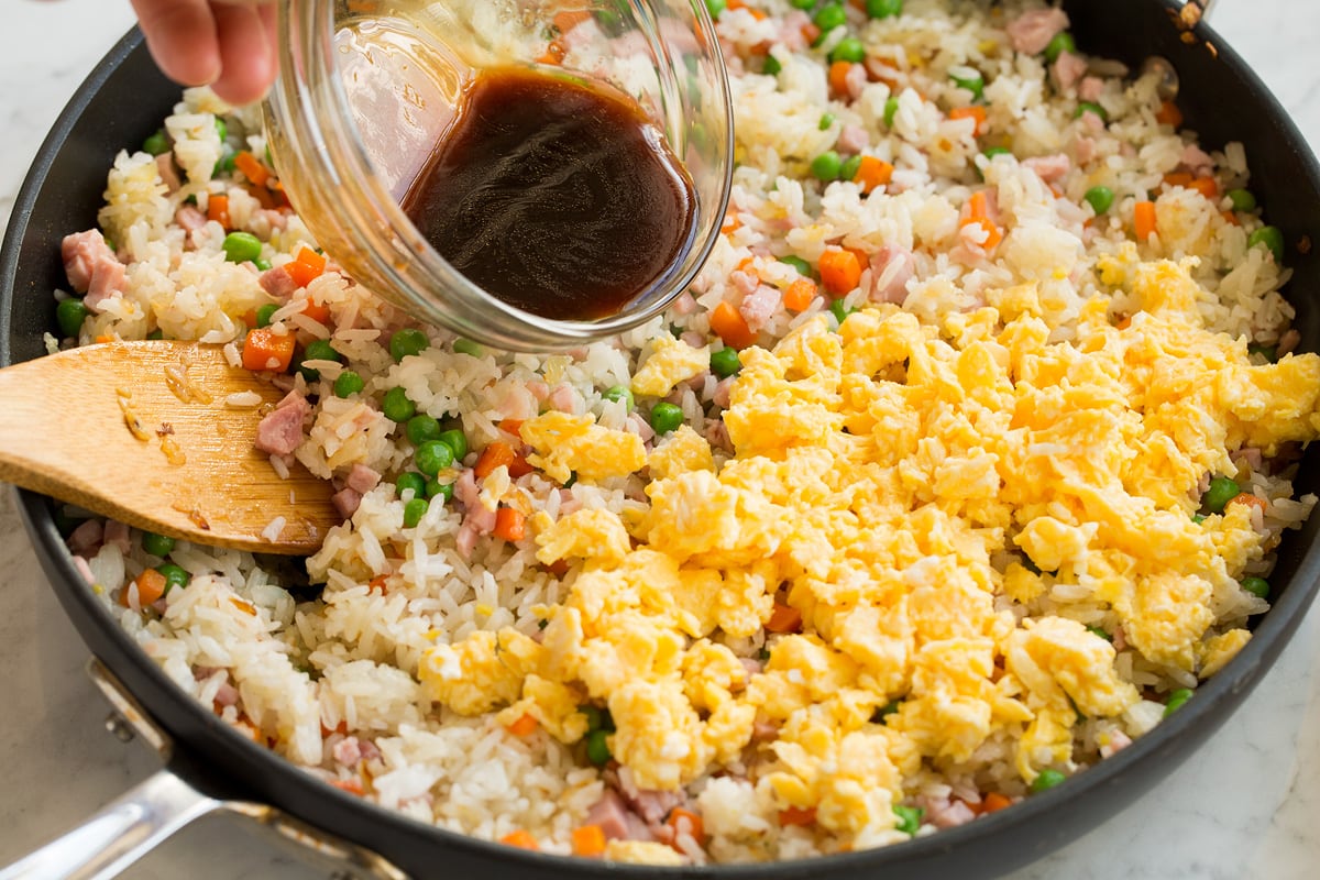 Scrambled eggs added to fried rice mixture in pan.