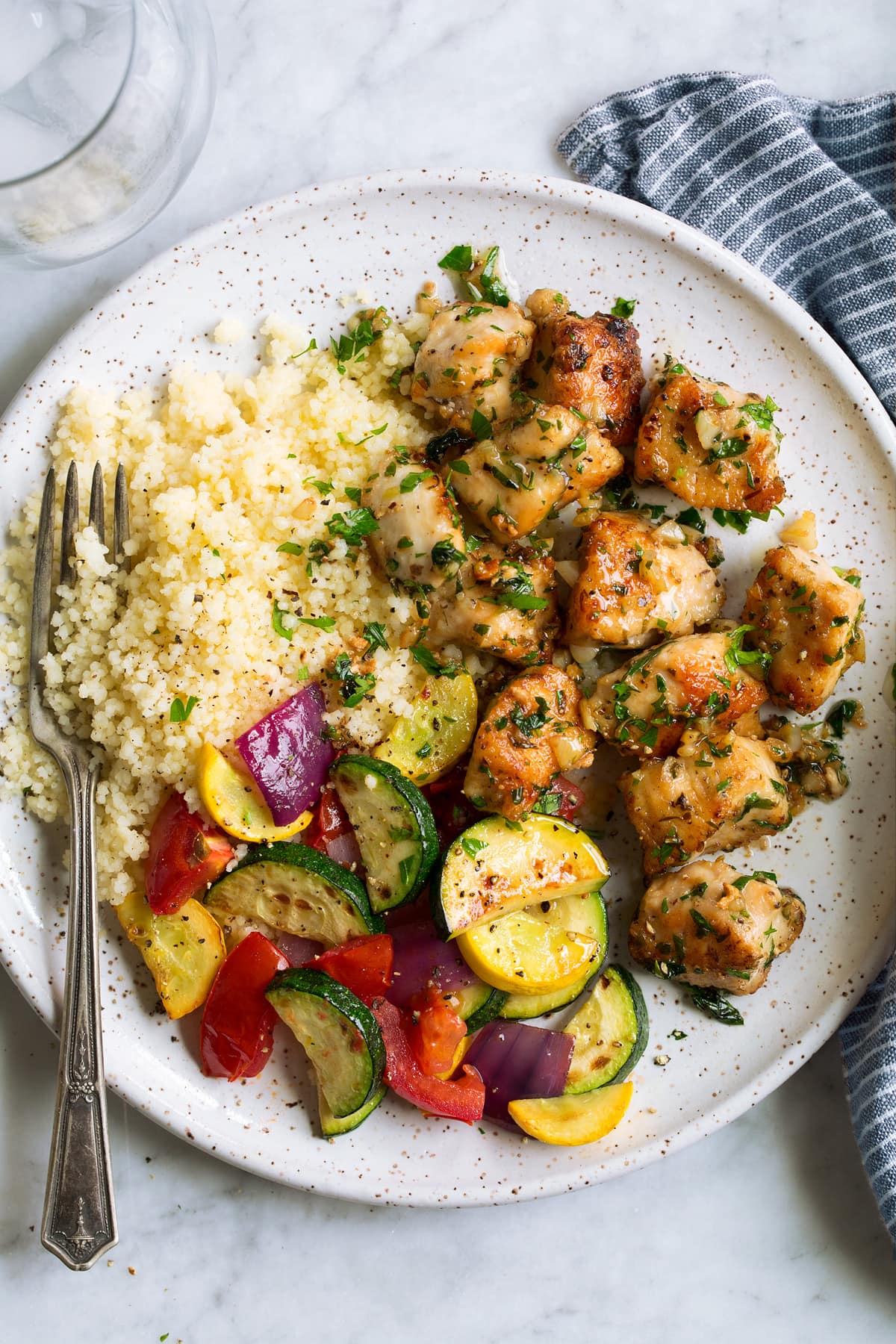 Garlic butter chicken bites on a plate with a side of couscous and fresh sauteed vegetables.